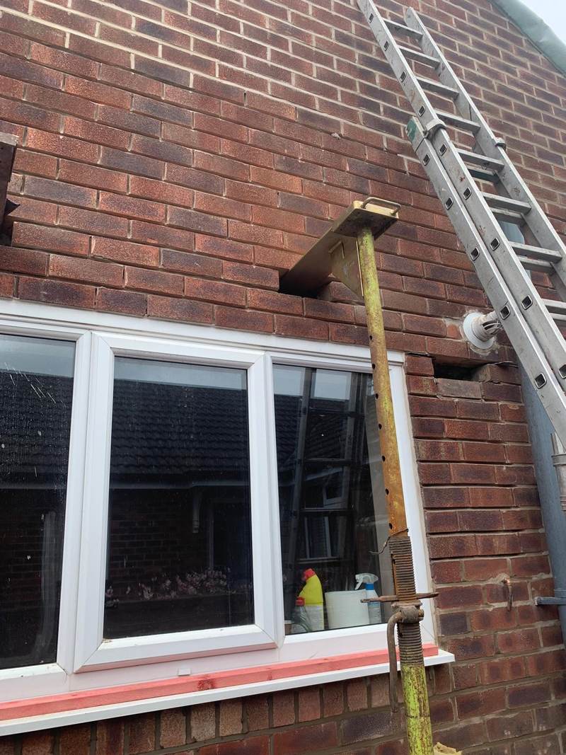 Brickwork repair beside a window with a temporary support prop in Bolton
